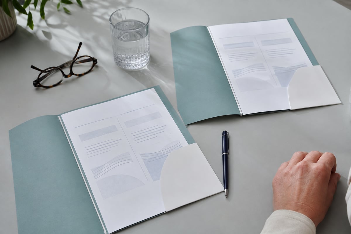 Information folders, reading glasses and a pen laid out for comparison